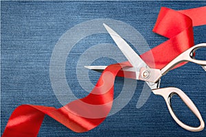 Scissors cutting red ribbon, close-up view on blue