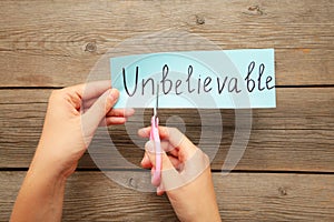 Scissors cutting white paper with the text unbelivable, change word to belivable. Hand holding card with the text unbelievable