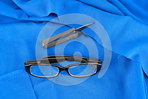 Scissors and glasses on blue cloth background