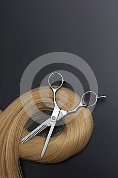 Scissors and piece of blond hair. Professional barber hair cutting shears on black background. Hairdresser salon equipment concept
