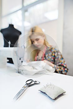 Scissors and pillow with needles on the background of seamstresses working in the workplace