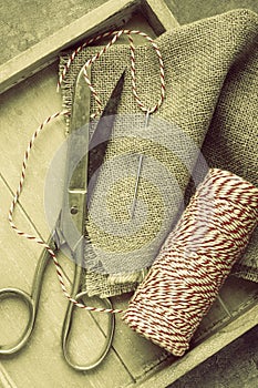 Scissors, spool of thread, needle and sackcloth on wooden tray