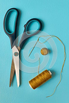 Scissors, spool of thread, needle and thimble on cyan background