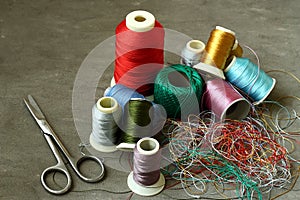 Scissors, tangled colored threads and spools of thread are on the concrete