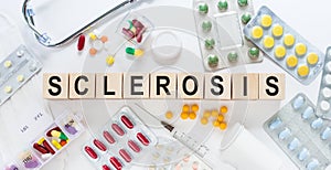 SCLEROSIS word on wooden blocks on a desk. Medical concept with pills, vitamins, stethoscope and syringe on the background