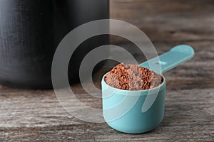 Scoop of chocolate protein powder on wooden table
