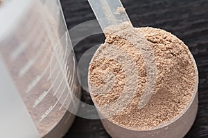 Scoop of chocolate whey isolate protein in front of protein shaker and its parts