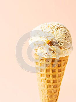 Scoop of delicious salted caramel toffee vanilla ice cream in waffle cone on pastel peachy pink background. Summer desserts photo
