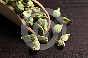 Scoop with dry cardamom pods on wooden table, closeup