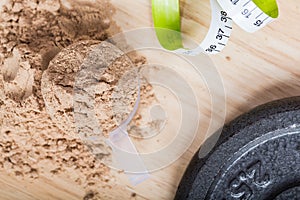 Scoop of whey protein on a wooden plate with measure tape.