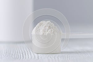 A scoop with white powder closeup and a jar on gray background