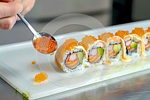 scooping roe with a spoon to top a sushi roll