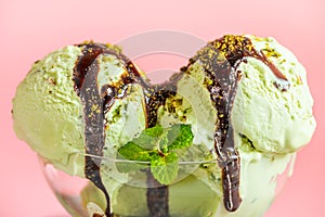 scoops green ice cream decorated chocolate topping, pistachio nuts and mint on pink background