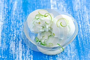 Scoops of lime ice cream with lemon zest, mint, in a bowl or plate on blue