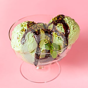 Scoops of pistachio ice cream decorated chocolate topping and nuts on pink background, top view