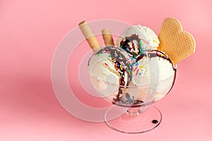 vanilla flavor ice cream in glass bowl with chocolate sauce, strewed sprinkles and waffle cookies on pink background