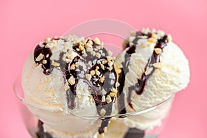 Scoops vanilla ice cream decorated chocolate topping and nuts on pink background