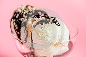 Scoops white ice cream decorated chocolate topping and nuts on vase over pink background