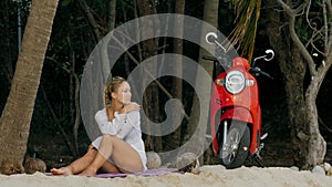 Scooter road trip. Woman alone on red motorbike in white clothes on sand beach by ocean. One girl caucasian tourist walk