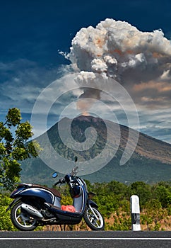 Scooter standing on the edge of the road with Mount Agung volcano dramatic eruption on background