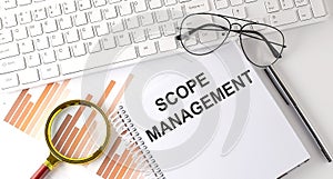 SCOPE MANAGEMENT text written on a notebook with keyboard, chart,and glasses