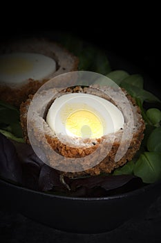 Scotch egg halved on lettuce leaves in a black dish.