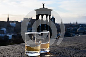 Scotch single malts or blended whisky spirits in glasses with Calton hill in Edinburgh on background, Scotland