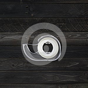 Scotch tape dispenser isolated on black wood background
