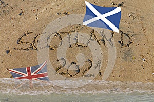 Scotland 2021 written in sand, Scottish flag up, British flag flooded by water