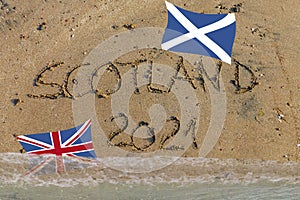 Scotland 2021 written in sand, Scottish flag up, British flag flooded by water