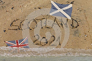 Scotland 2021 written in sand, Scottish flag up, British flag flooded by water