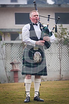 Scottish piper from Scotland in traditional outfit with tartan kilt playing bagpipe