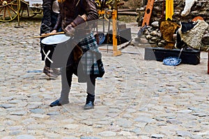 A Scottish warrior, soldier, musician in traditional costume with a skirt beats the drum on the square of a medieval old castle.