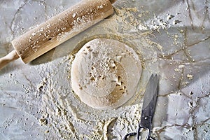 Scoured dough sprinkled with flour and wooden rolling pin and kitchen scissors on a marble table
