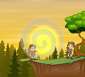 Scout boy and girl standing on mountain cliff of sunset background