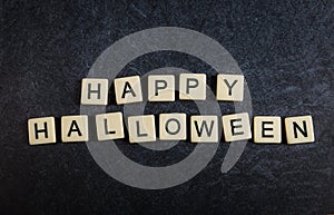 Scrabble letter tiles on black slate background spelling Happy Halloween