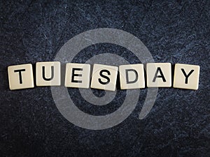 Scrabble letter tiles on black slate background spelling Tuesday