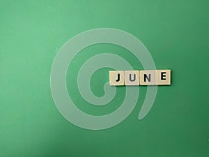 scrabble tiles spelling'june'in wood on a green wall