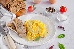 Scrambled eggs cooking from organic fresh eggs on a white plate with rye bread on a light background with a cup of coffee.