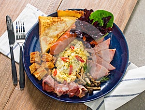 Scrambled eggs with fried bacon,ham,fried sausages,fries,mushroom, tomato and toast