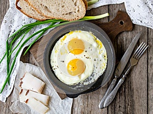 Scrambled eggs in frying pan with pork lard, bread and green feathers onions on old wooden table. National Ukrainian or