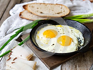 Scrambled eggs in frying pan with pork lard, bread and green feathers onions on old wooden table. National Ukrainian or