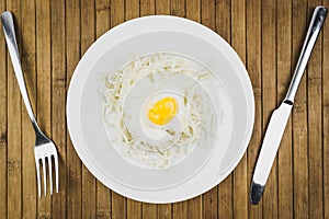 Scrambled eggs and spaghetti in plates, knives and fork on wooden table.