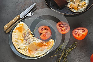 Scrambled eggs with tomato on a plate , knife and fork on a gray