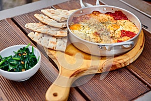 Scrambled eggs with tomatoes, cheese and spices in an aluminum frying pan with handles with homemade thin lavash and juicy greens