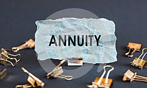 A scrap of blue paper with clips on a gray background with the text - ANNUITY. Conceptual photo fixed sum of money paid to someone