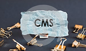 A scrap of blue paper with clips on a gray background with the text - CMS