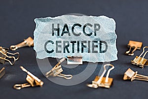 A scrap of blue paper with clips on a gray background with the text - HACCP CERTIFIED