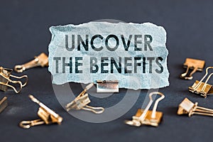 A scrap of blue paper with clips on a gray background with the text - UNCOVER THE BENEFITS