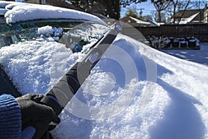 Scraping snow off of car windshield - hand in glove and telescoping ice scraper with shadows - selective focus